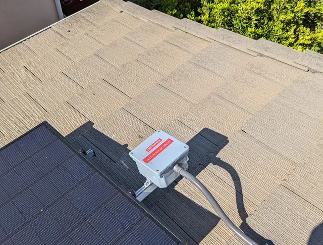 A junction box mounted at the edge of a solar module with the conduit leaving the array across a concrete tile roof, Long Beach
