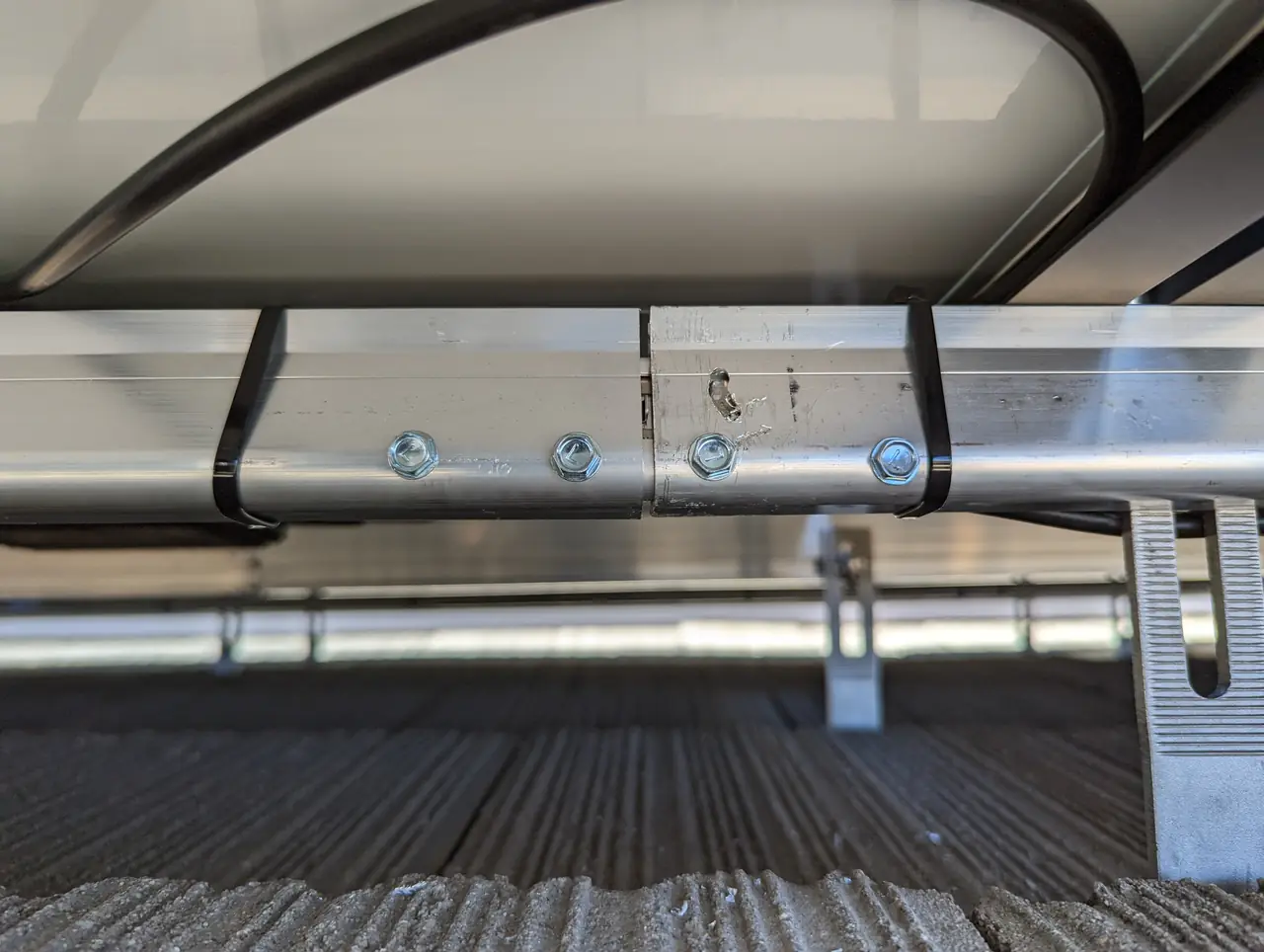 The underside of a solar array showing an aluminum rail, a splice and the cable tied along it above a concrete tile roof, Long Beach