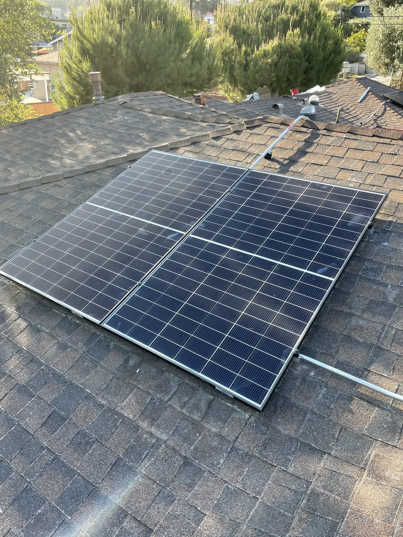 Two solar modules set near the ridge of a composition shingle roof with trees beyond, El Sereno, Los Angeles