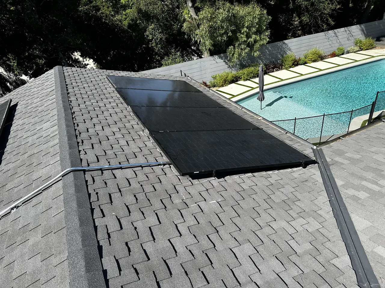 A solar array on a composition shingle roof above a garden and swimming pool, Brentwood, Los Angeles