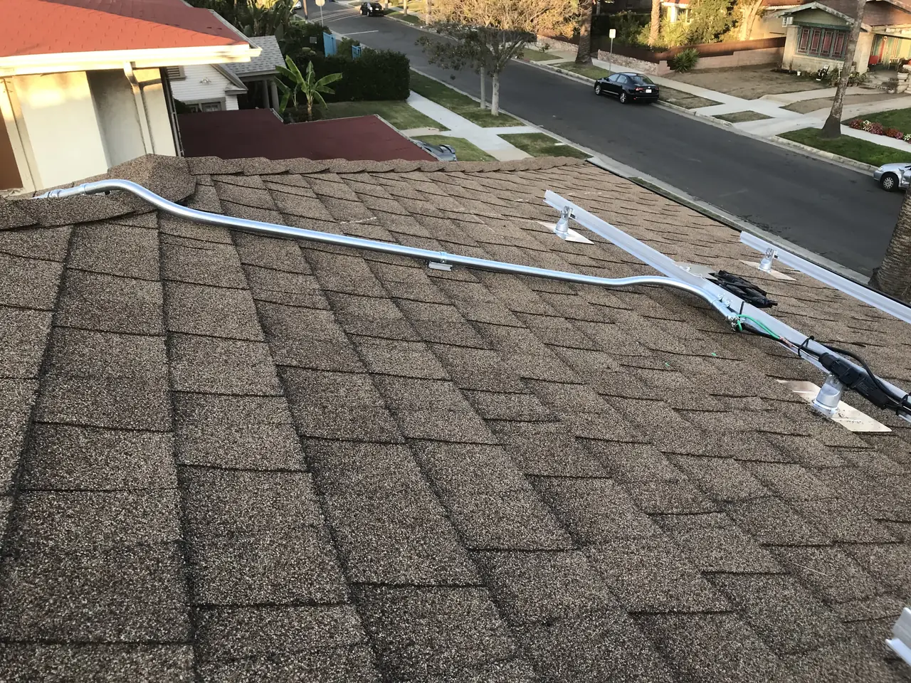 A conduit run fixed along a composition shingle roof slope above a street, West Adams, Los Angeles