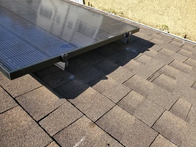 A solar module mounted on a composition shingle roof beside a stucco wall, Los Feliz, Los Angeles