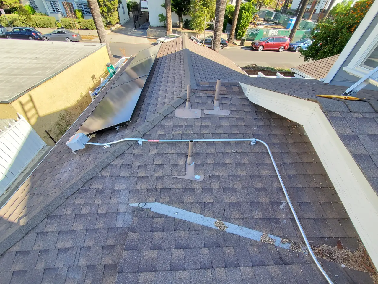 A conduit run fixed along a shingle roof ridge above a street, Los Feliz, Los Angeles