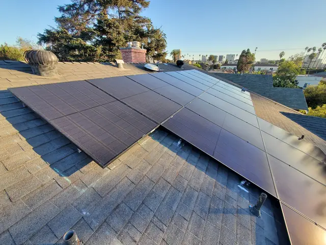 Solar modules across two planes of a composition shingle roof with trees and a distant skyline, Hancock Park, Los Angeles