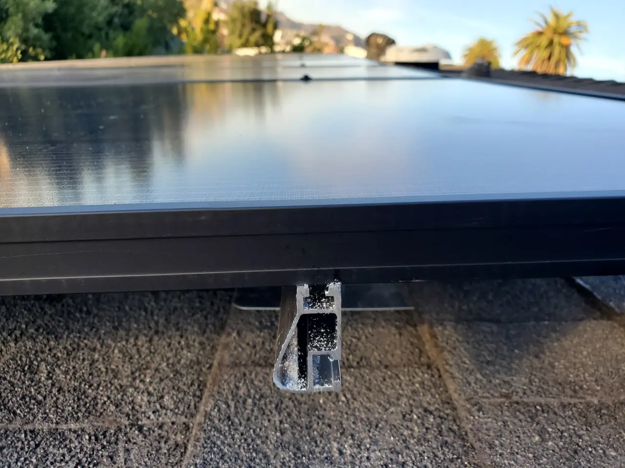 The edge of a solar module and its mounting foot seen close up on a shingle roof, Hancock Park, Los Angeles