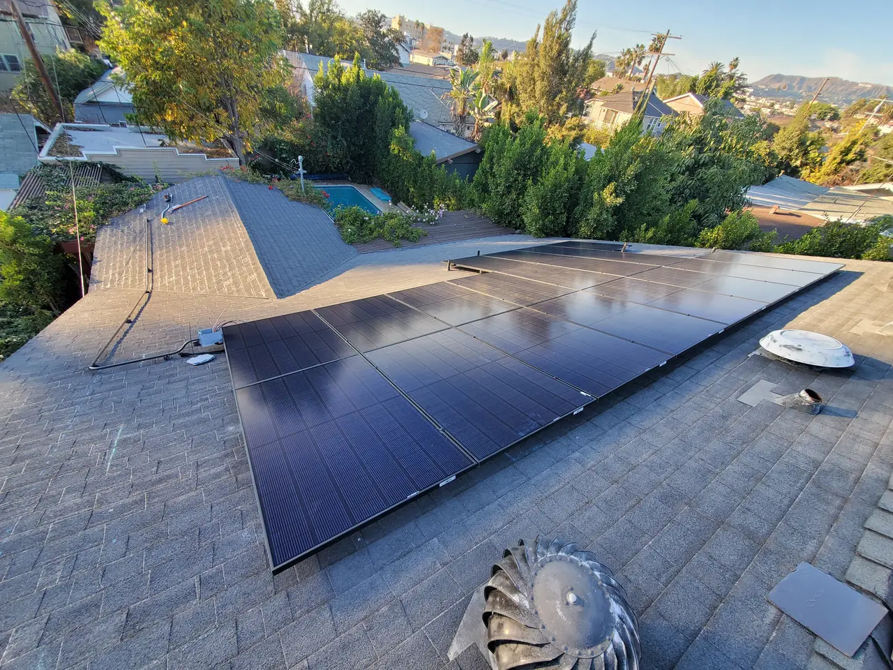 A solar array seen from above across a hipped shingle roof with hills beyond, Hancock Park, Los Angeles