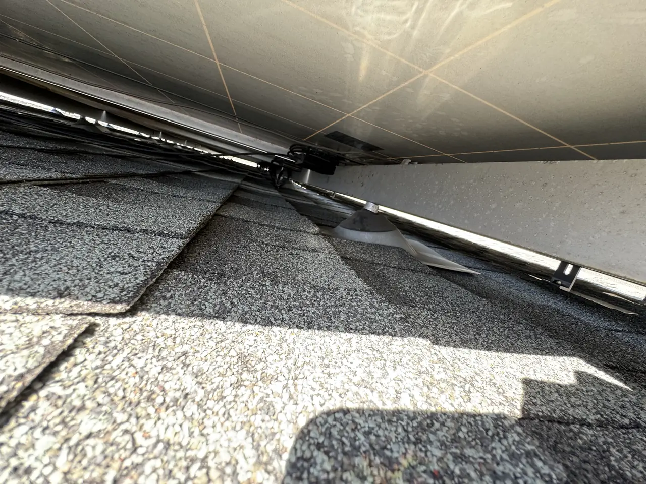 Direct-current cable lying across roof shingles beneath a solar module, Windsor Square, Los Angeles