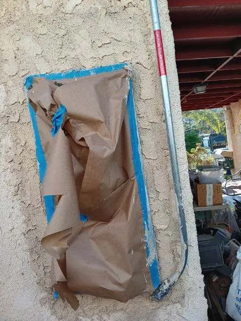 A stucco wall masked off with tape and paper around a patch where equipment had been removed, El Sereno, Los Angeles