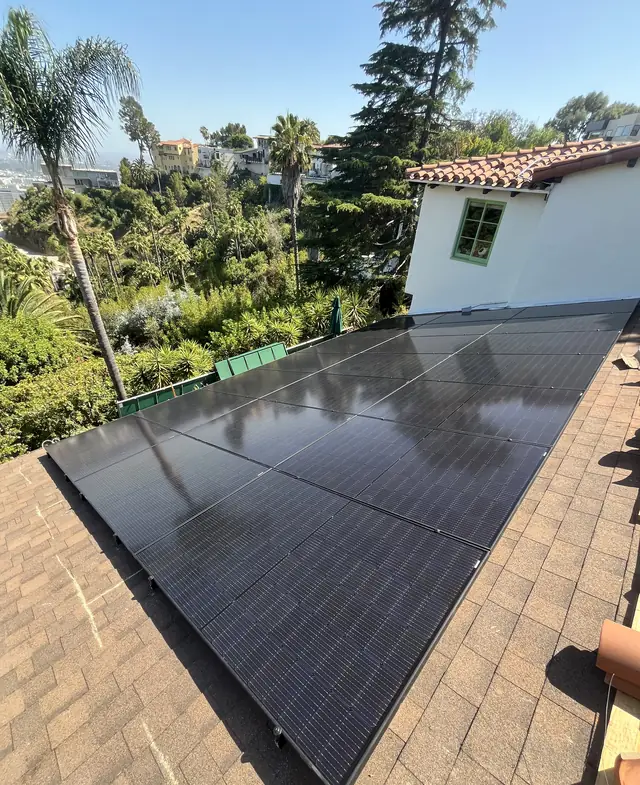 A black solar array on a tile roof where the tile has been removed, with palms beyond, Hollywood Hills, Los Angeles