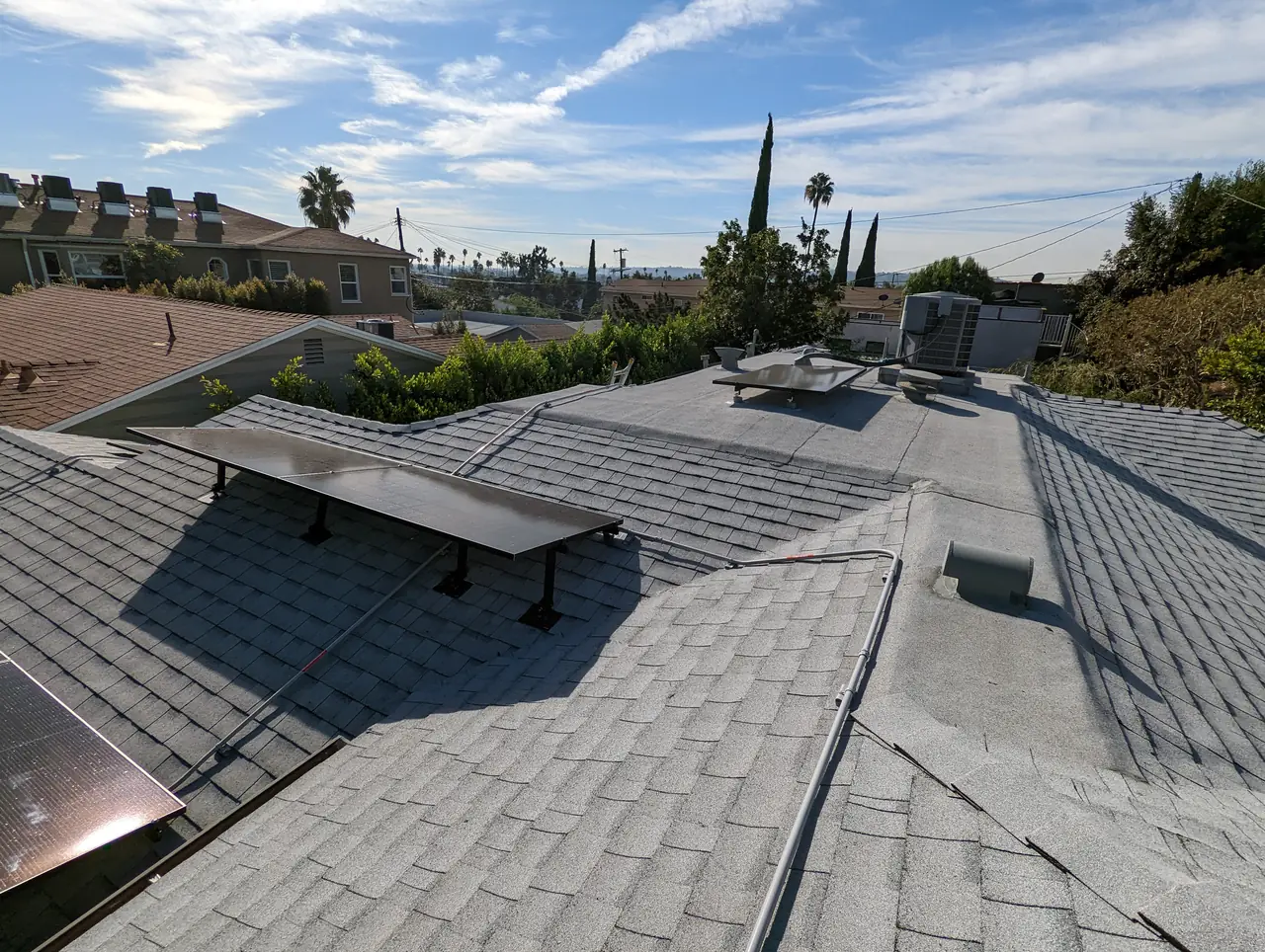 Solar modules on one plane of a hipped composition shingle roof with trees and blue sky beyond, Mid-City, Los Angeles