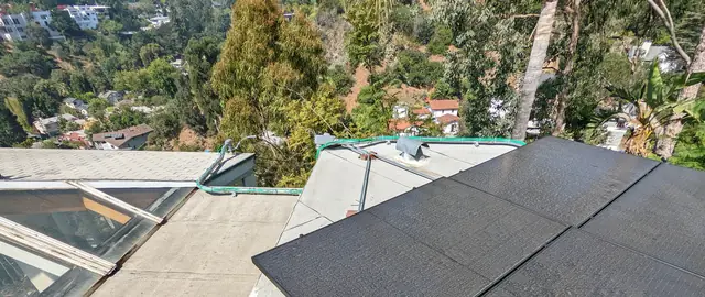 Solar modules on a low-slope roof section beside a skylight, with the hillside and neighboring houses beyond, Hollywood Hills, Los Angeles