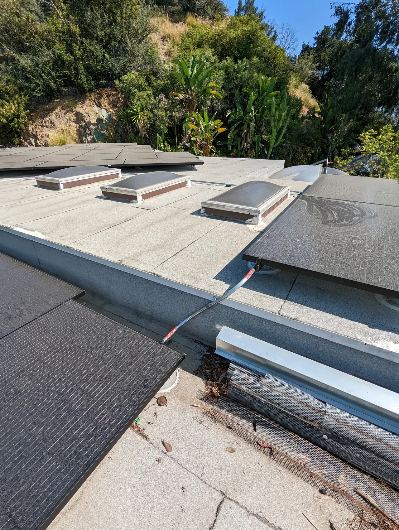 Solar modules across a low-slope roof with skylights and the hillside beyond, Hollywood Hills, Los Angeles
