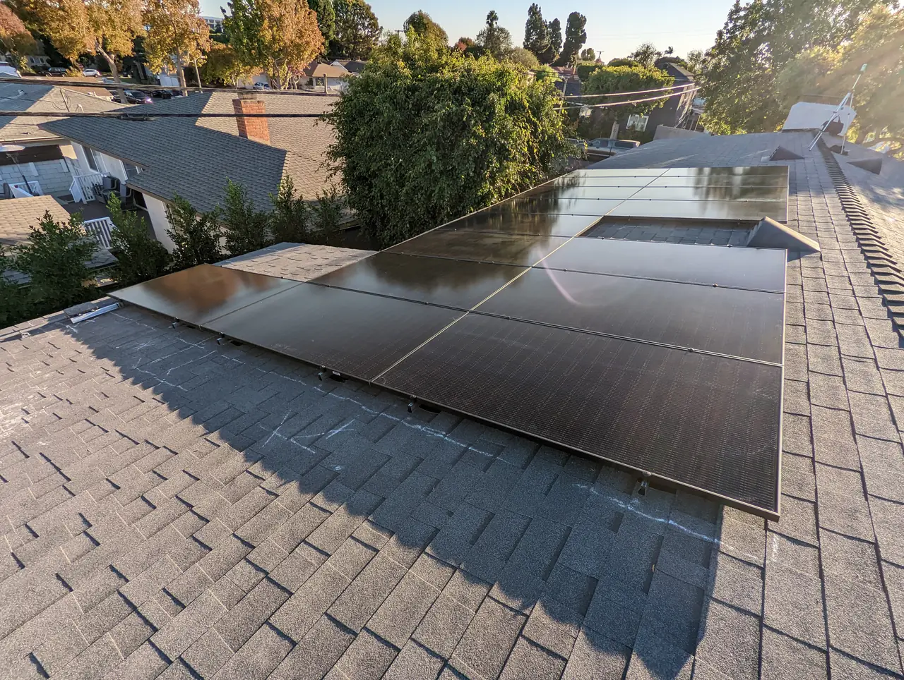 A completed solar array on a composition shingle roof with trees and a residential street beyond, Westchester, Los Angeles