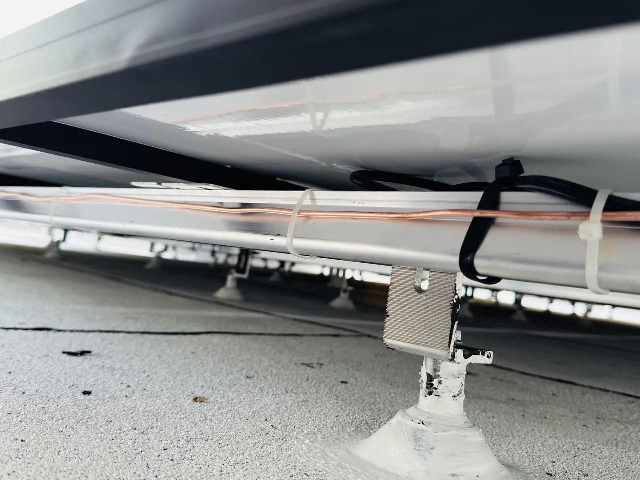 Mounting rails and feet seen from beneath a solar array on a low-slope roof, Brentwood, Los Angeles