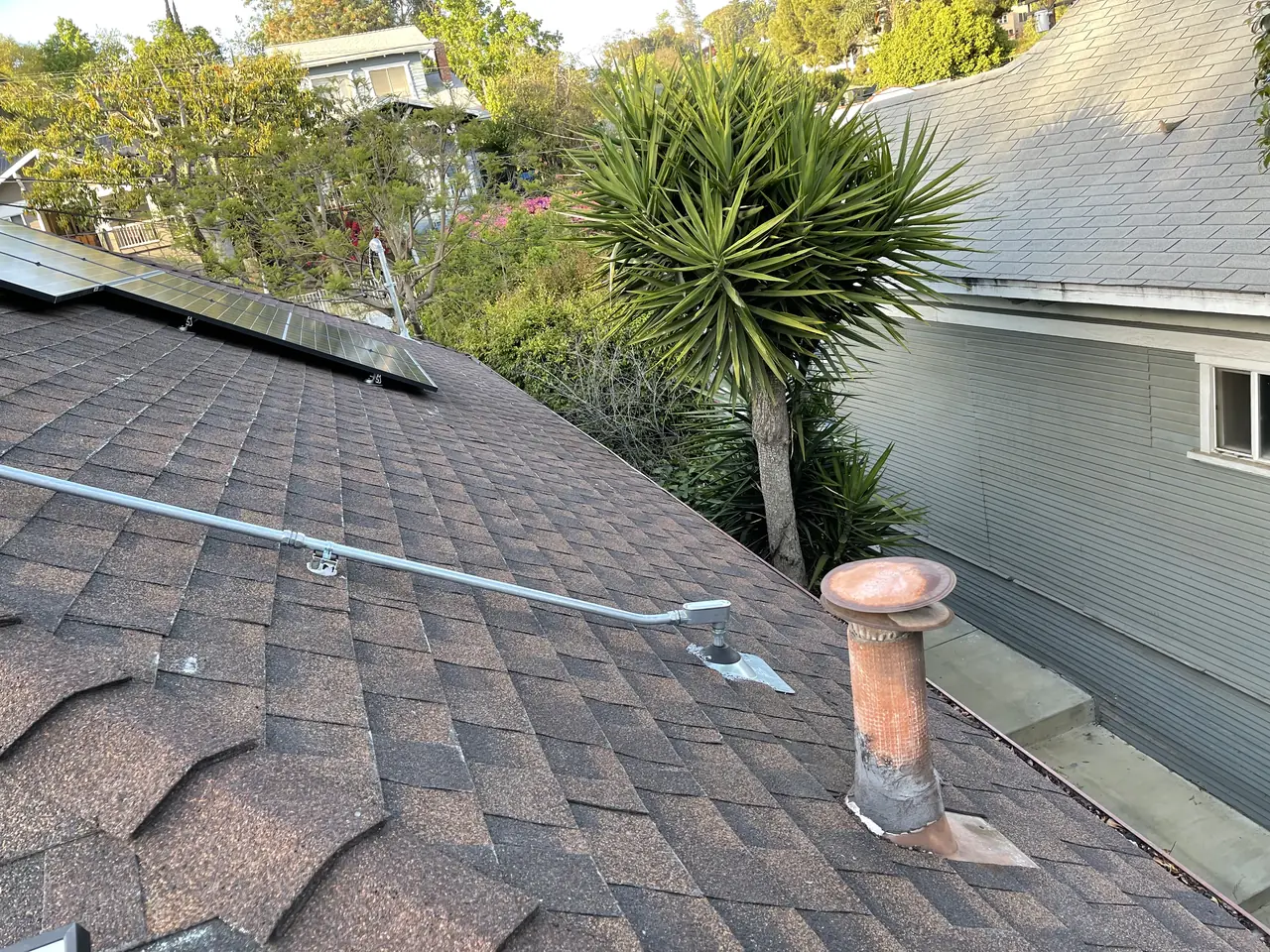 A finished solar array on a hipped composition shingle roof with hillside houses behind, Echo Park, Los Angeles