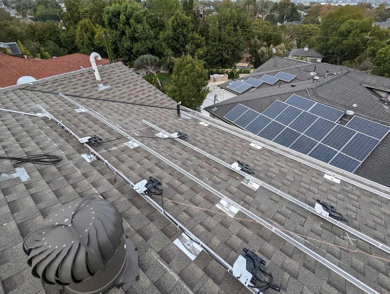 Mounting rails laid out on a composition shingle roof with a neighboring array visible beyond, Palms, Los Angeles