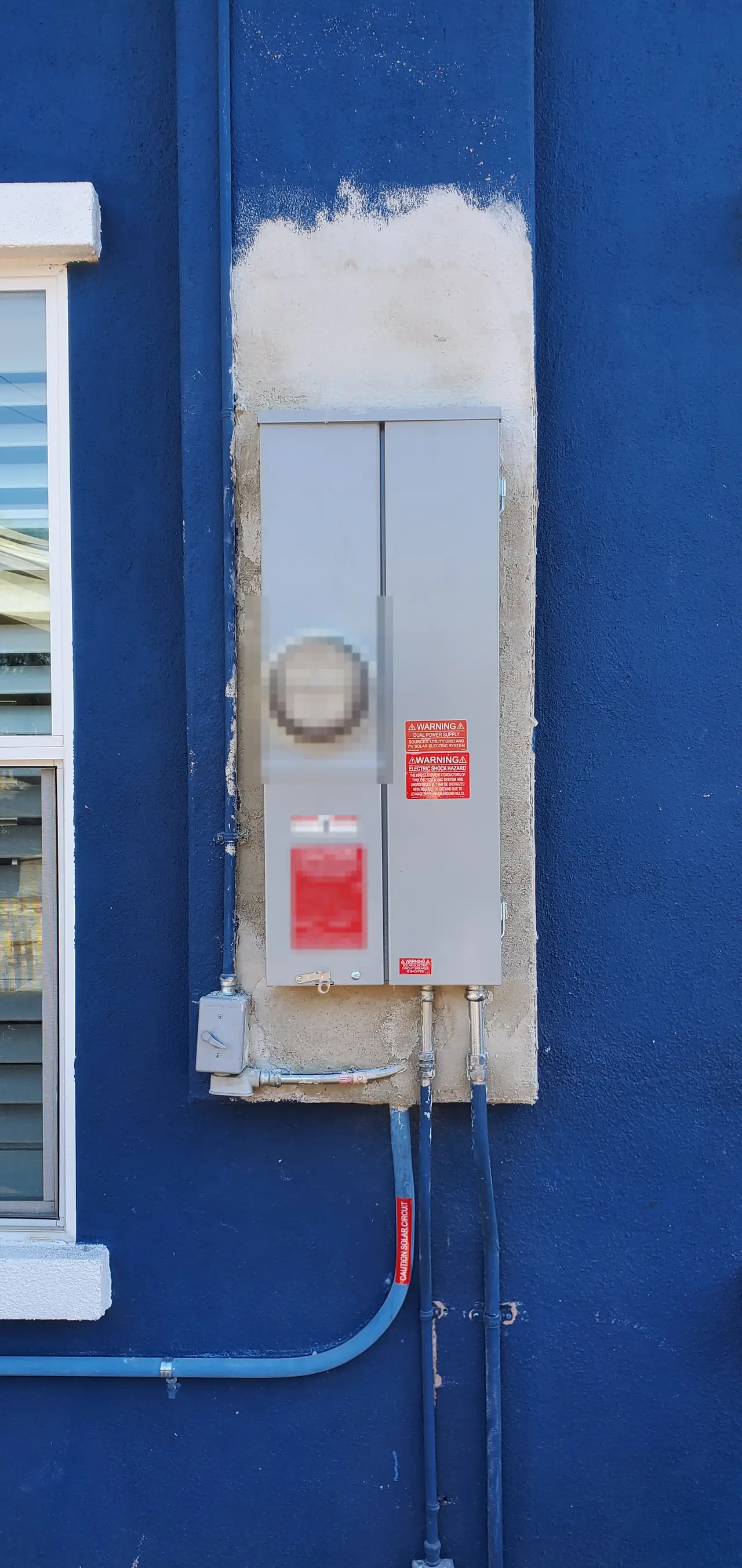 A gray meter and service panel in a fresh patch of stucco on a blue wall, with conduit running down, Mission Hills