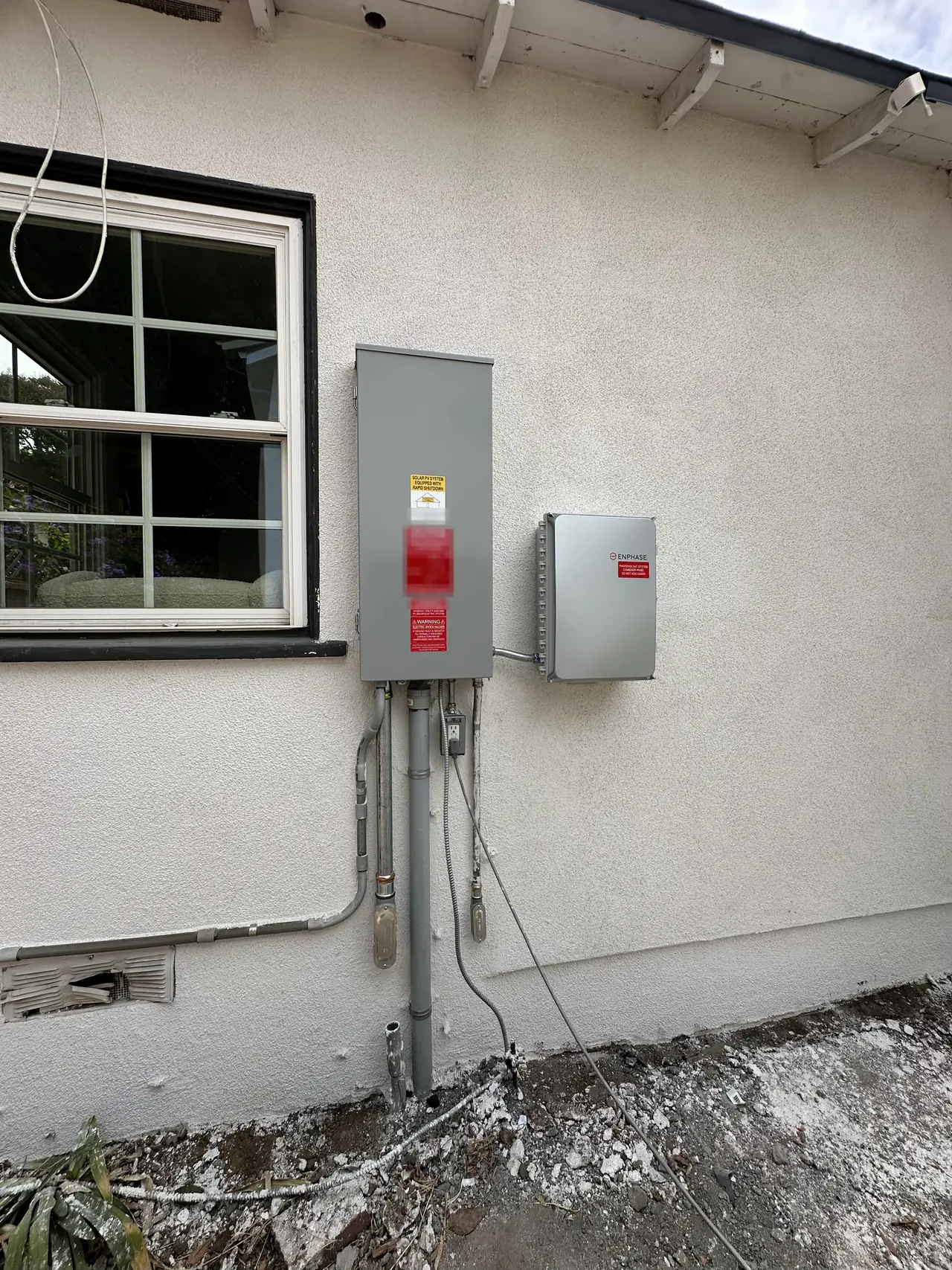 A gray electrical enclosure with solar placards and an Enphase combiner box on a white stucco wall, Mission Hills