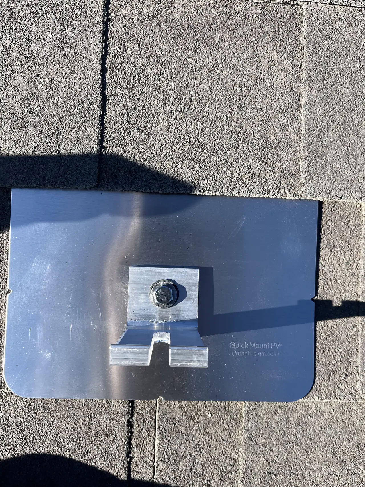 A flashed solar mount with its foot bolted down, set under a gray shingle course, Mission Hills