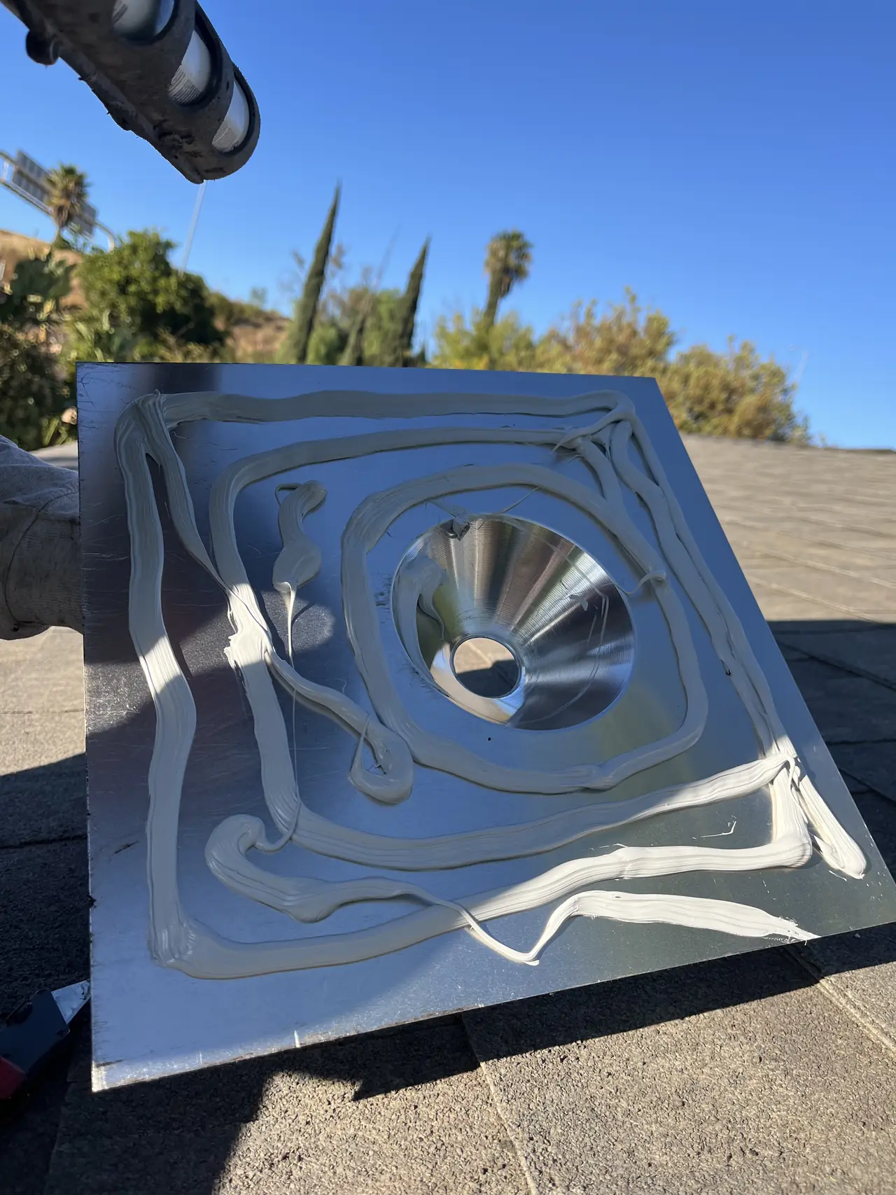 Rings of sealant on the underside of a metal roof flashing for a conduit, held up over a shingle roof, Mission Hills