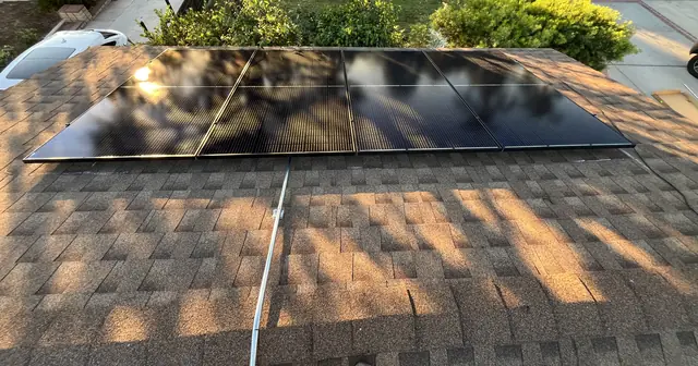 A row of four black solar modules on one face of a brown shingle hip roof in late afternoon light, Mission Hills