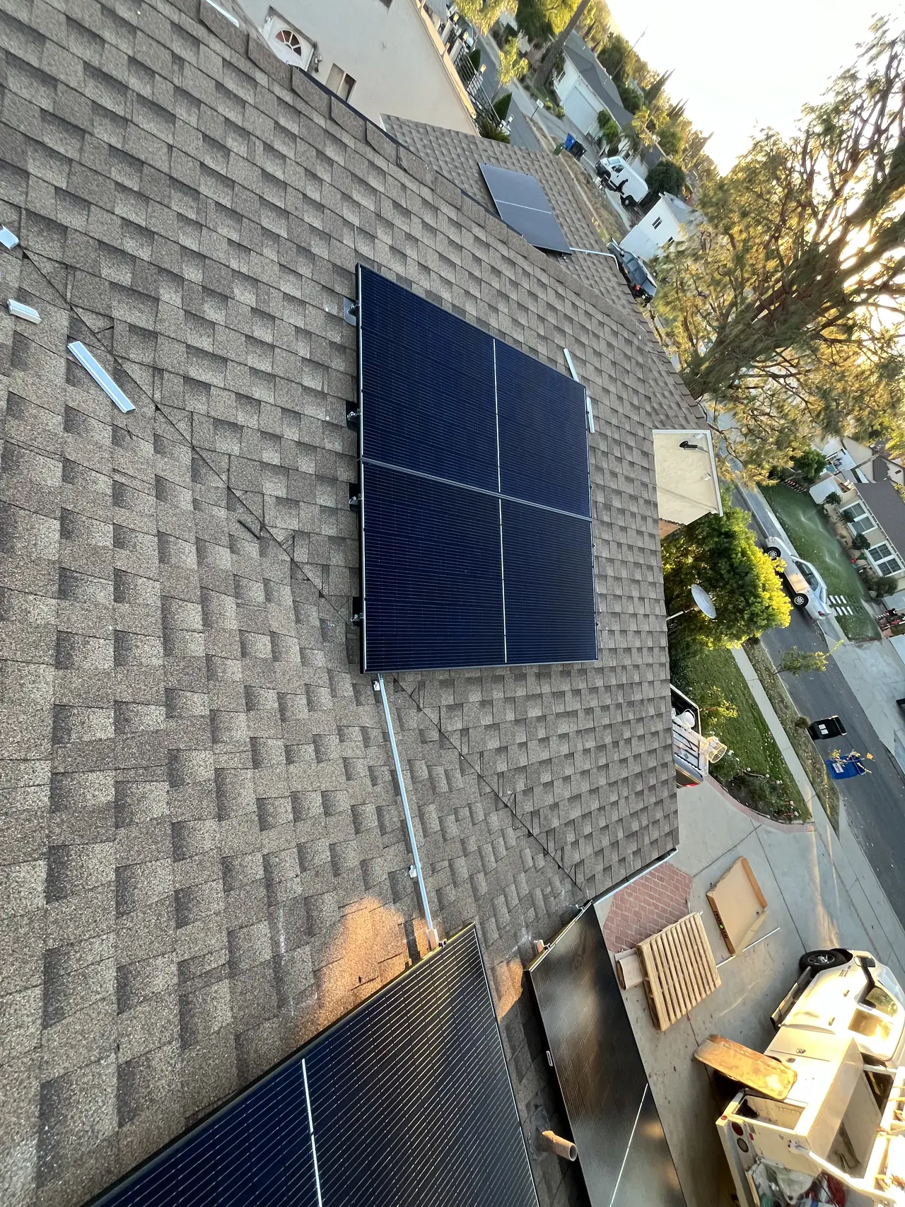A block of four solar modules on one face of a brown shingle hip roof, with trees and houses below, Mission Hills