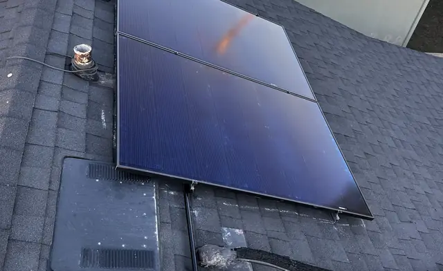 Two dark solar modules newly set on a composition shingle roof beside the ridge, North Hills, Los Angeles