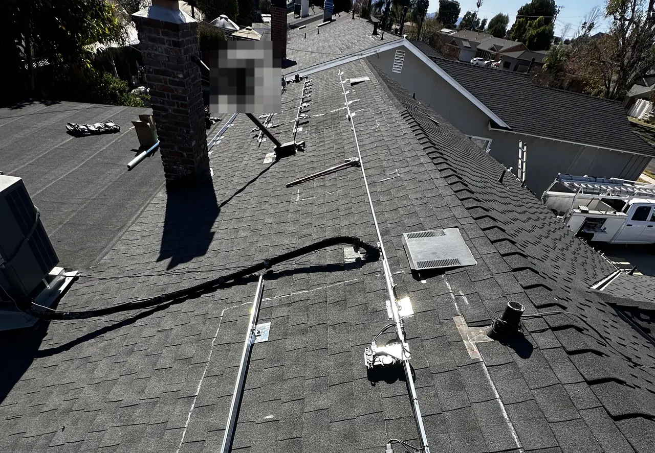 Aluminum mounting rails running along a shingle roof toward a chimney, with a suburban street beyond, North Hills, Los Angeles