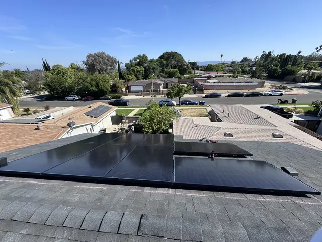 Black solar modules in an L shape on a hip roof with the surrounding neighborhood behind, North Hills, Los Angeles