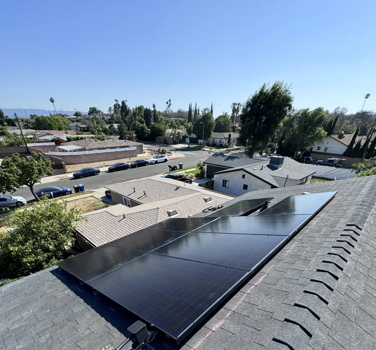 Black solar modules following the slope of a shingle roof with the neighborhood and hills beyond, North Hills, Los Angeles