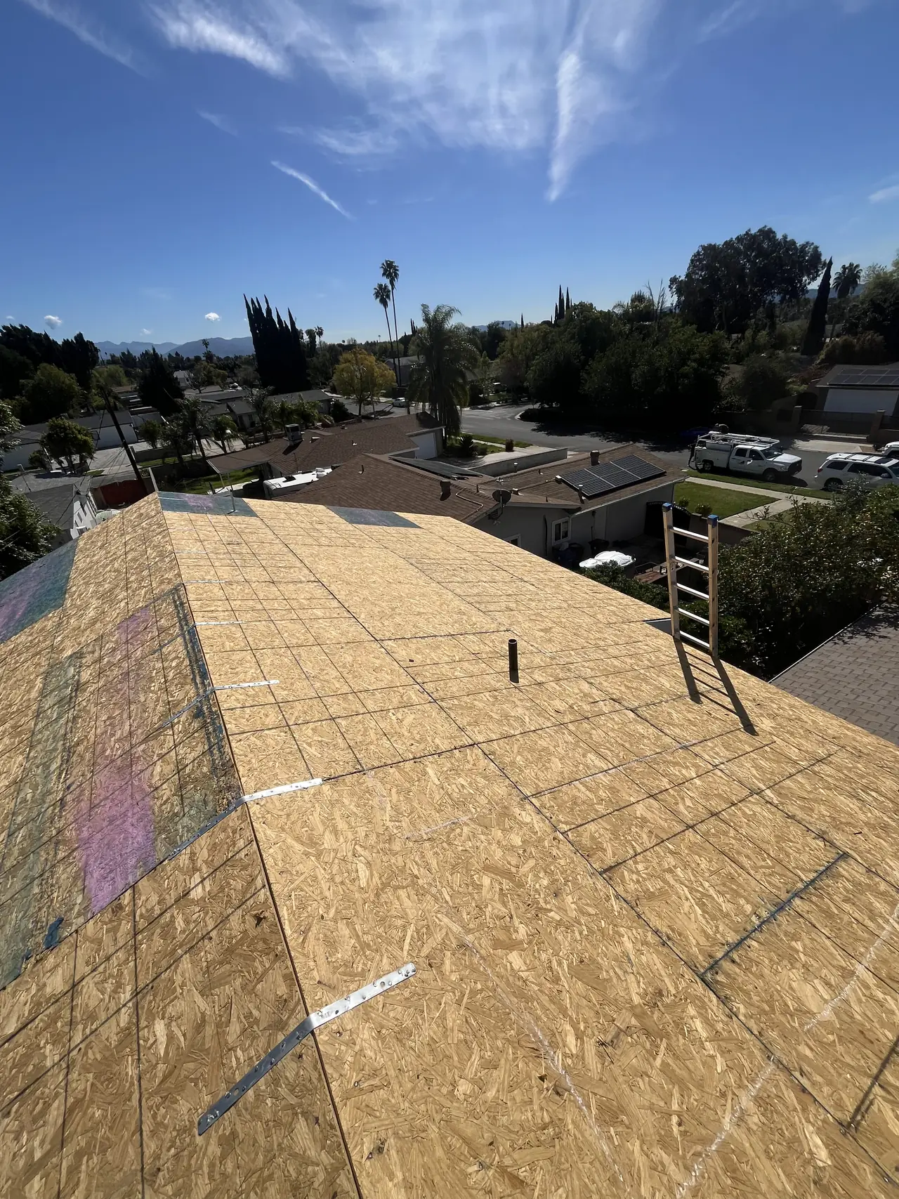 The bare OSB sheathing of a new dwelling's roof before the shingles go on, with rooftops beyond, North Hills, Los Angeles