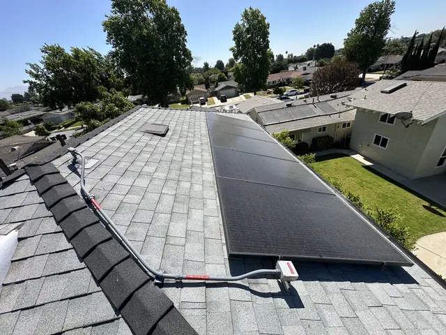 A solar array on a shingle roof with neighboring yards and trees beyond, North Hills, Los Angeles