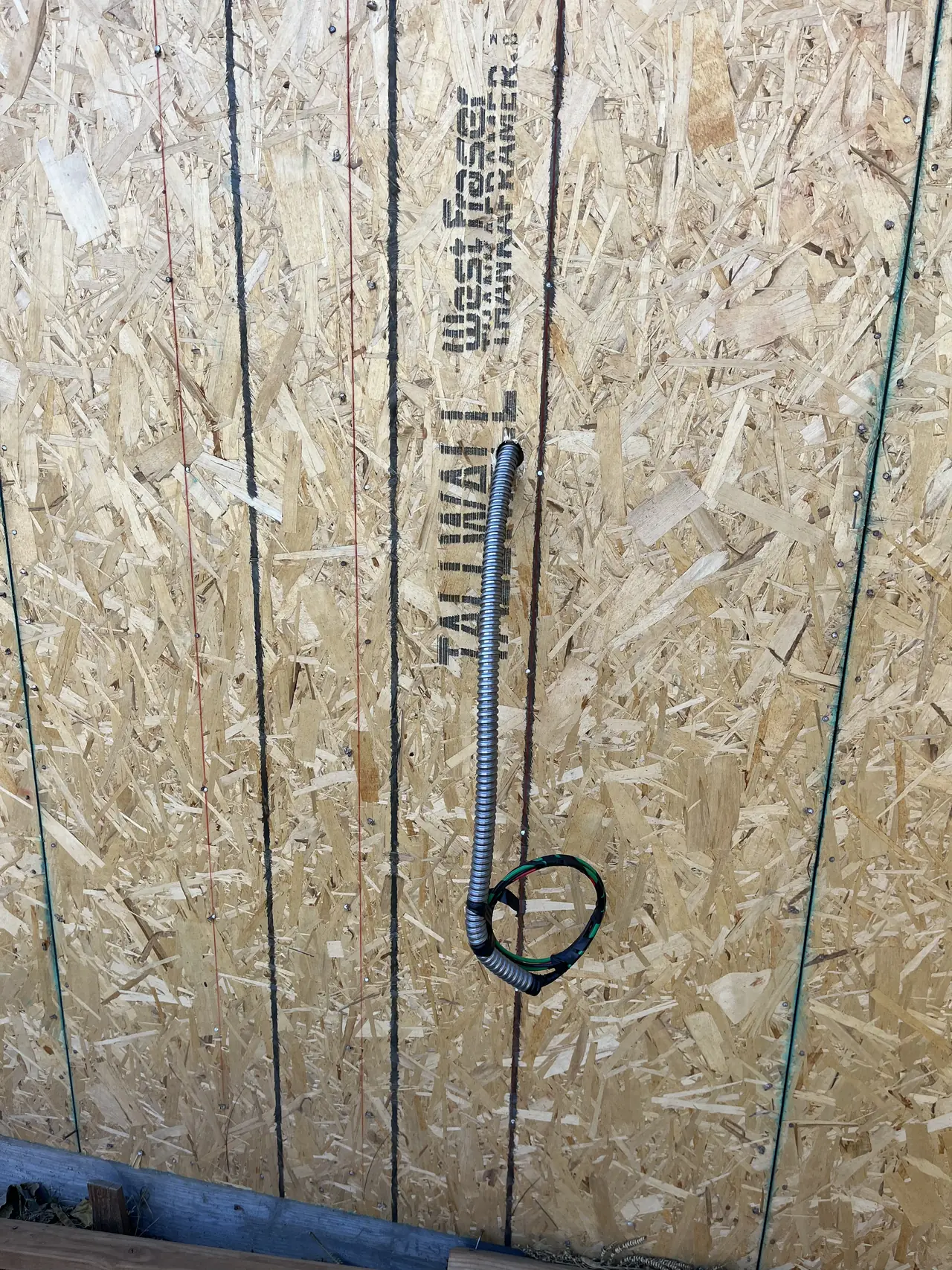Flexible conduit and a coiled wiring whip on the sheathed outer wall of a new dwelling, North Hills, Los Angeles