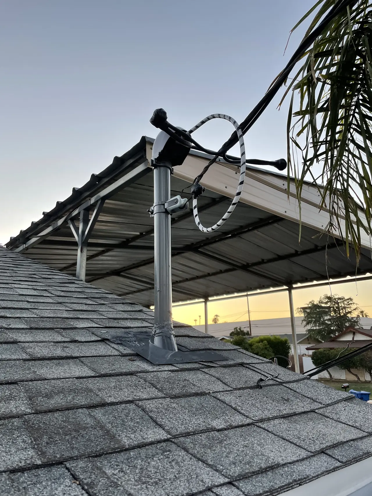 A mounting upright and conduit whip on a shingle roof at dusk, beside an existing shade structure, North Hills, Los Angeles