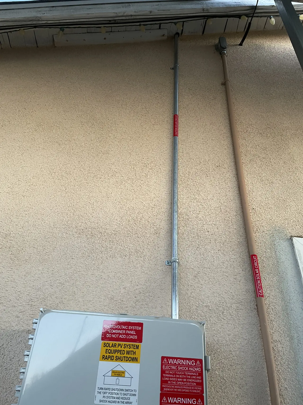 A vertical conduit run down a stucco wall to a solar combiner enclosure, North Hills, Los Angeles