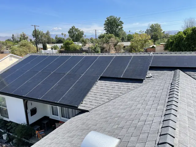 A solar array spread across two planes of a shingle roof with the valley and distant hills beyond, North Hills, Los Angeles