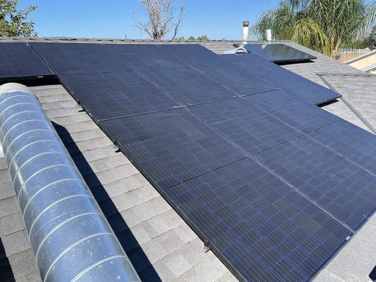 A row of solar modules along a shingle roof slope with ductwork running beside them, North Hills, Los Angeles