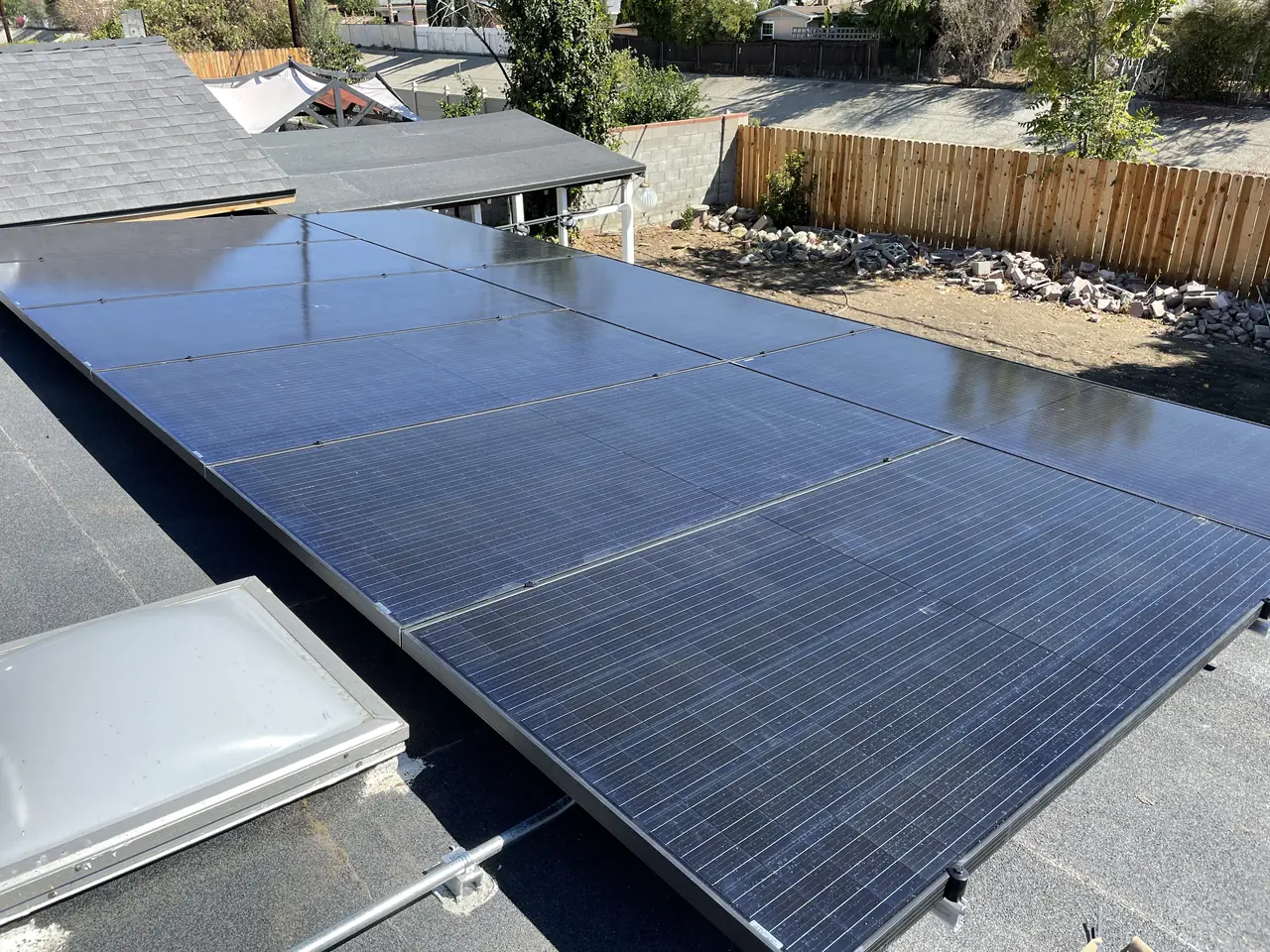 Solar modules lying almost flat on the low-slope section of a roof above a fenced yard, North Hills, Los Angeles