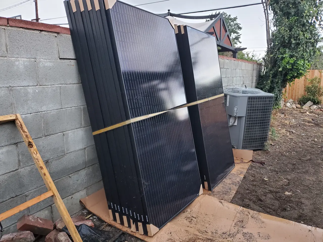 Solar modules stacked upright against a concrete block wall in a side yard before installation, North Hills, Los Angeles