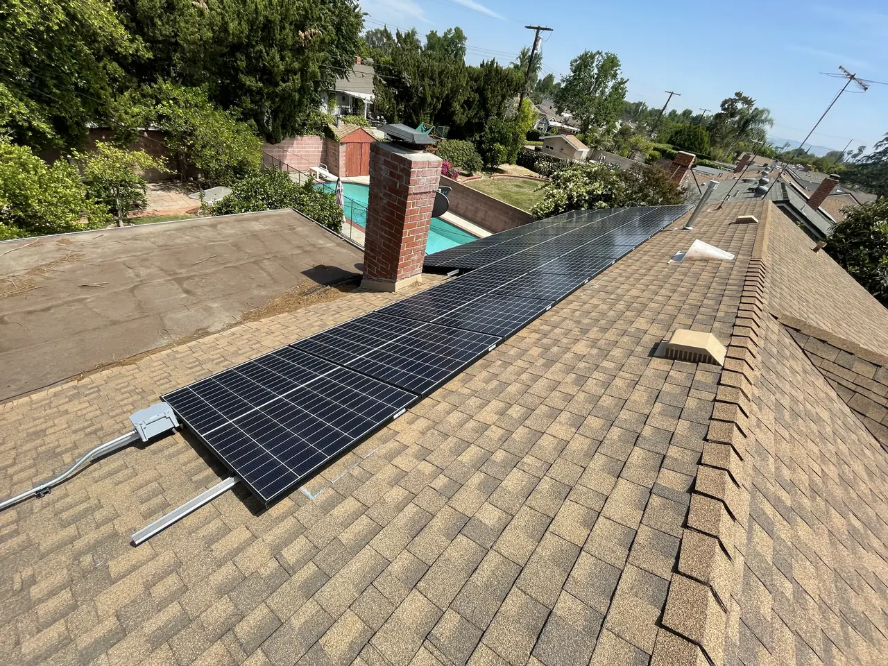 A second group of solar modules on the far plane of a shingle roof with trees and neighboring rooftops, North Hills, Los Angeles