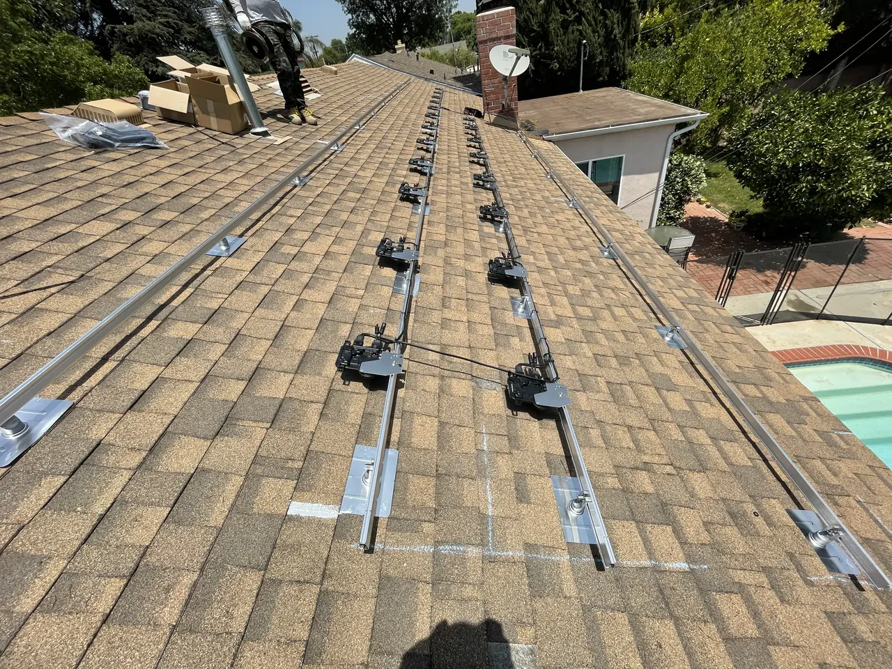 Aluminum mounting rails fixed along a shingle roof with a chimney behind and a pool in the yard, North Hills, Los Angeles