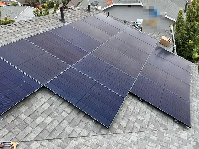 A solar array spanning two planes of a shingle roof above a suburban street in the late afternoon, North Hills, Los Angeles