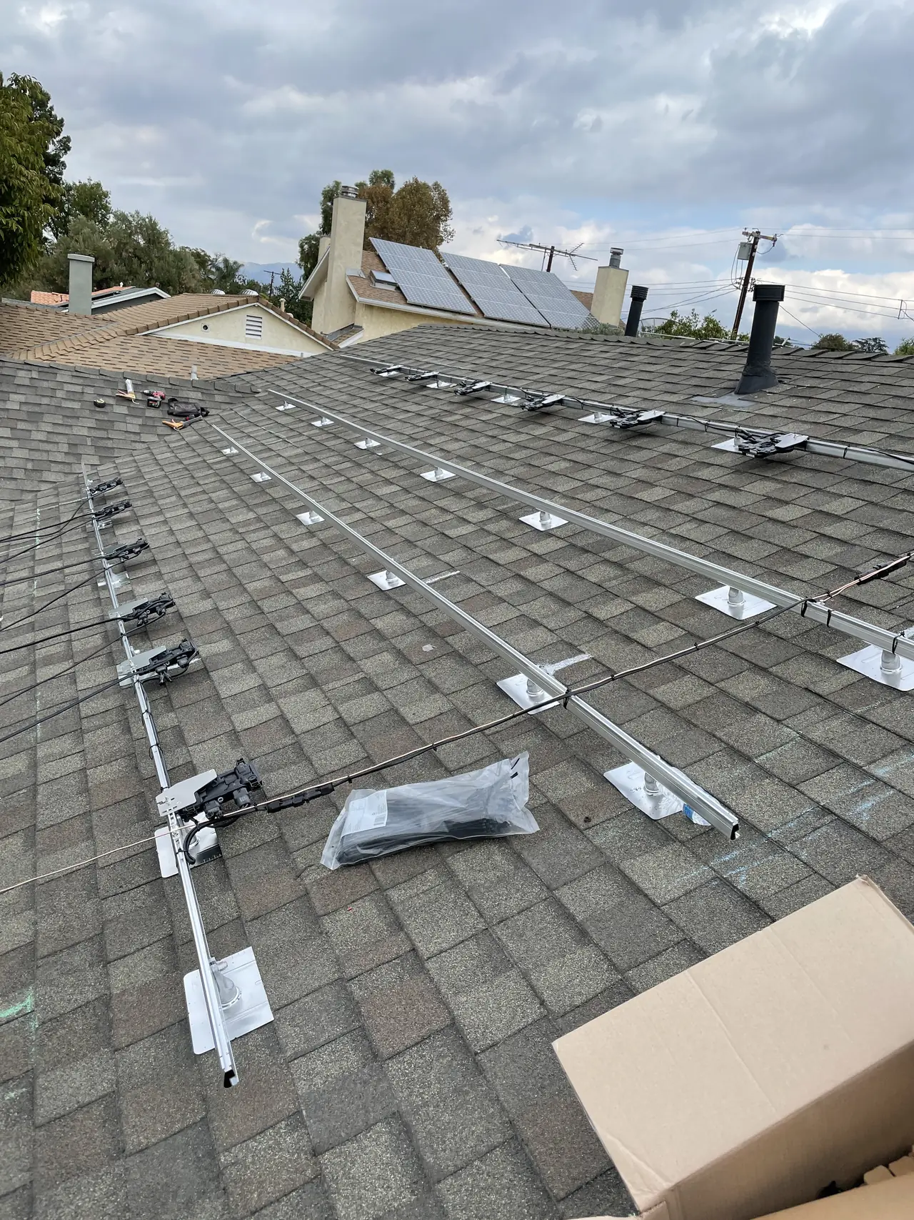Aluminum rails and mounting hardware laid out across a shingle roof before the modules arrive, North Hills, Los Angeles