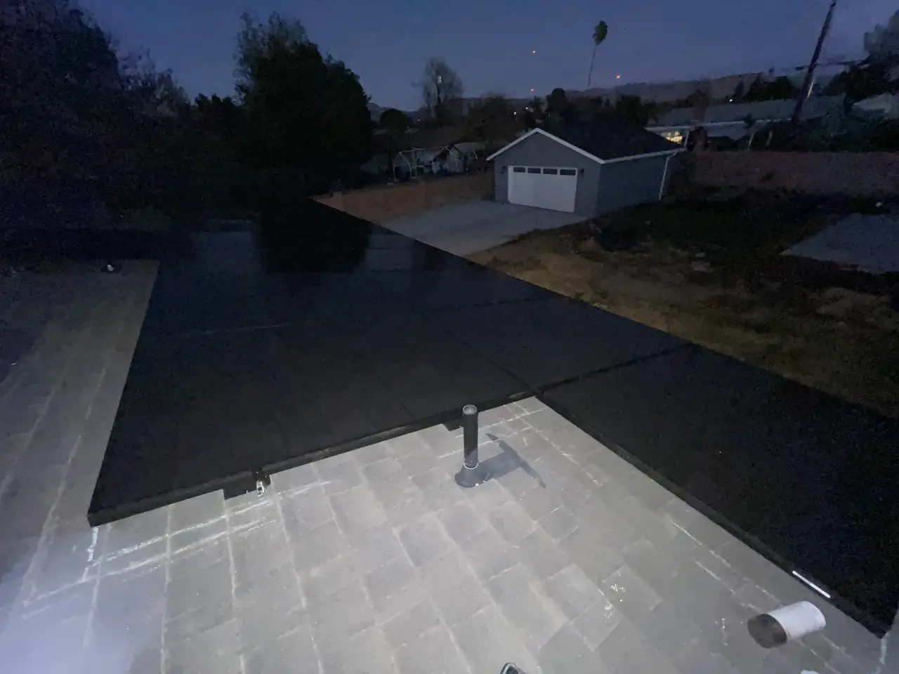 A solar array on a shingle roof photographed at dusk with a detached garage and the last light behind it, North Hills, Los Angeles