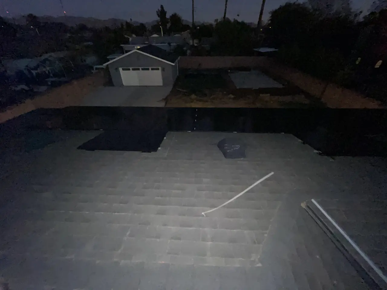 A solar array on a shingle roof in the last light of the afternoon with a detached garage beyond, North Hills, Los Angeles