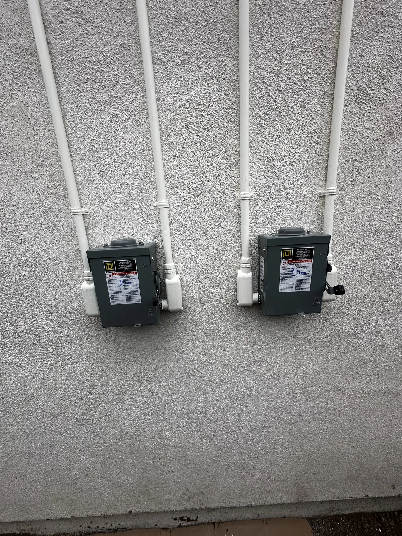 Two identical AC disconnects side by side on an exterior wall, each with its own pair of conduits, North Hollywood