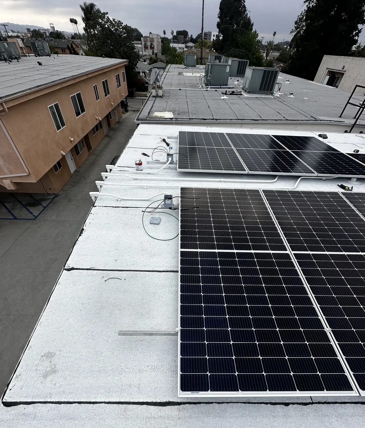 Finished solar arrays across a white flat roof with an apartment building alongside, North Hollywood
