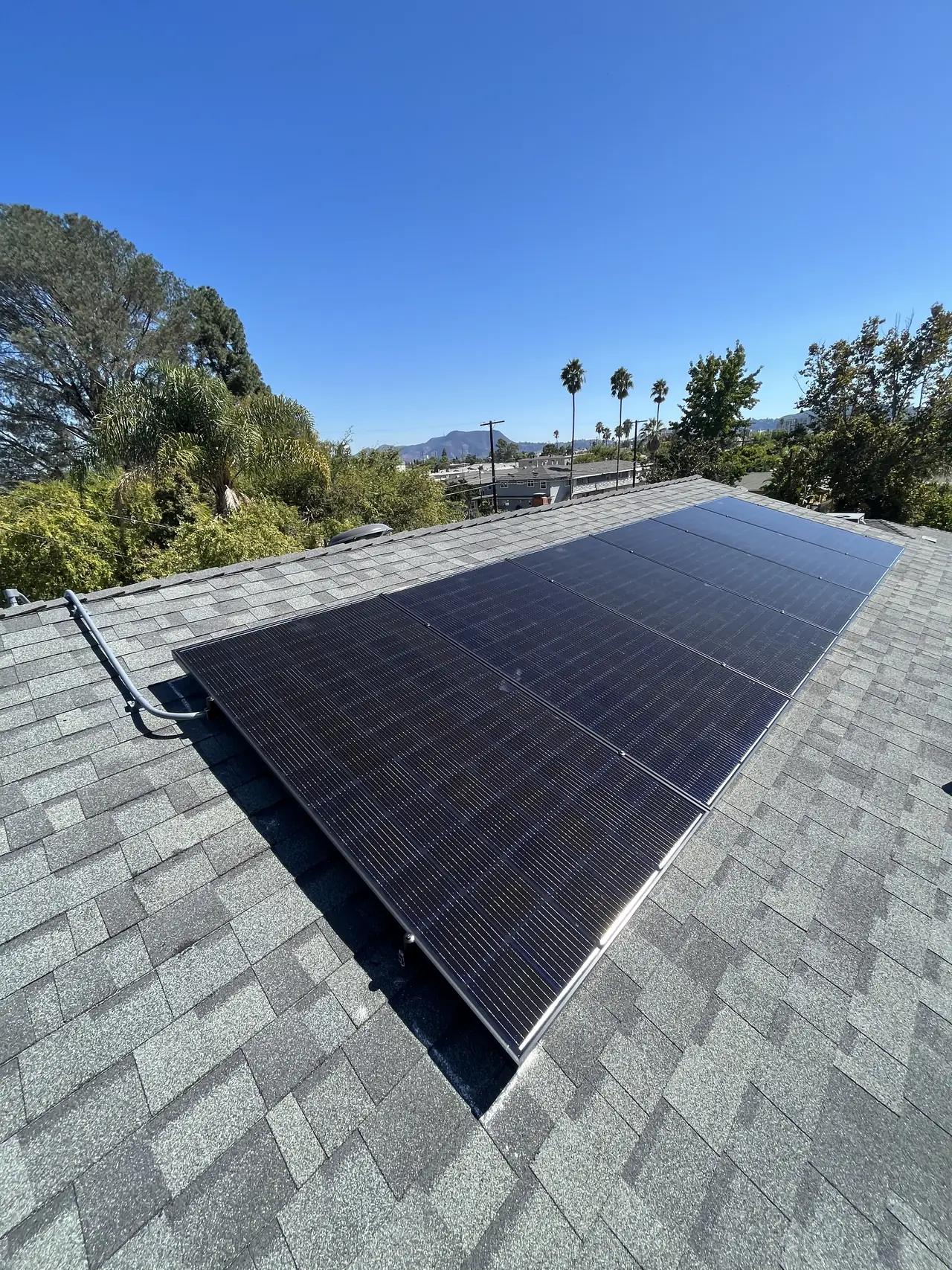 Finished solar array across a shingle roof with trees and hills behind, North Hollywood