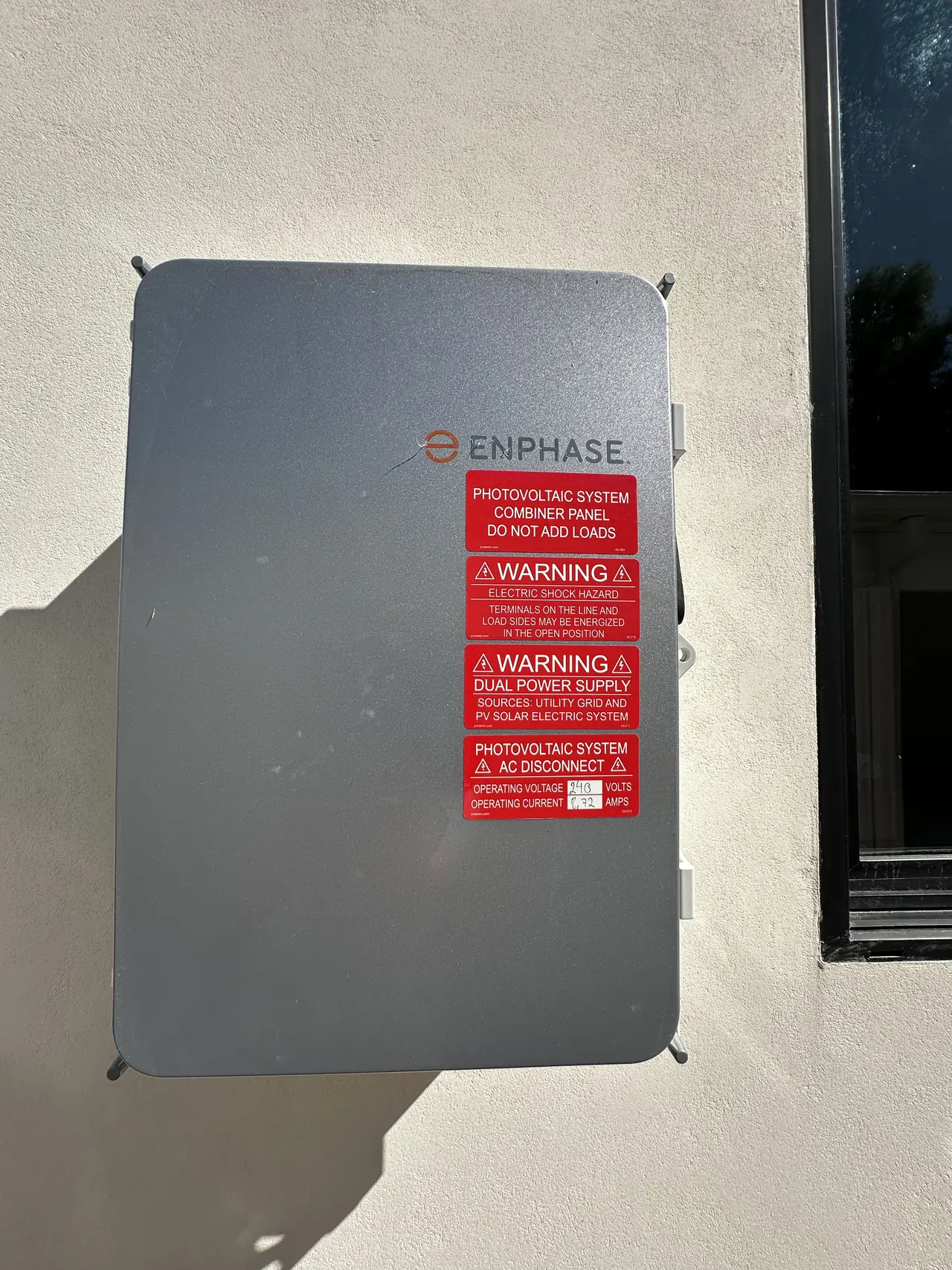 Enphase solar combiner panel mounted on a stucco wall with warning placards, North Hollywood