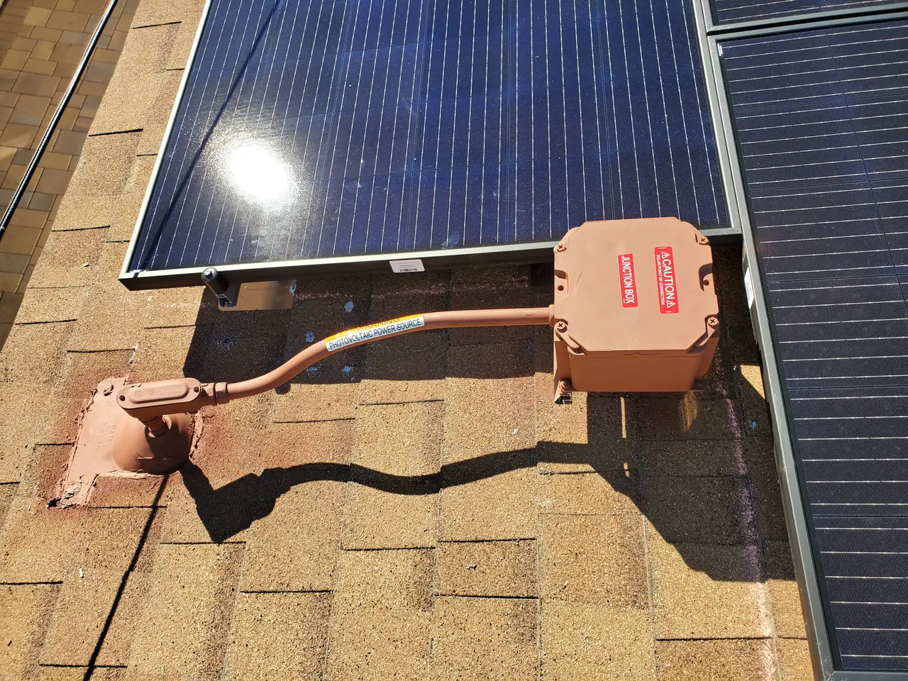 A solar module lifted to show the roof junction box and conduit beneath it, painted to match the shingle, North Hollywood